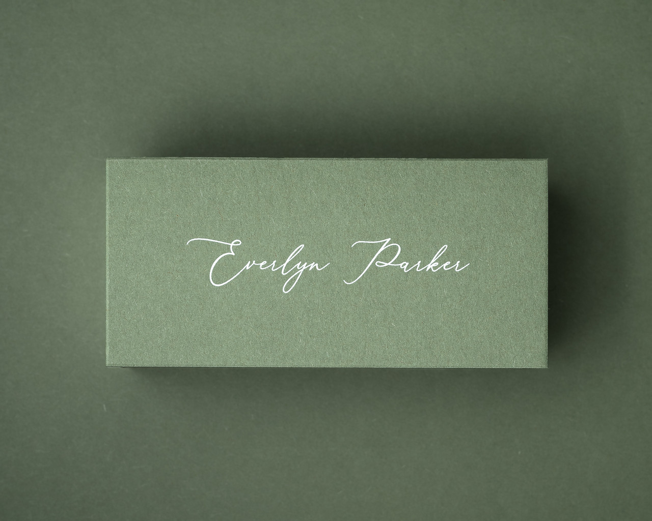 Olive green flat place card with white ink printed name in the same elegant handwritten style.