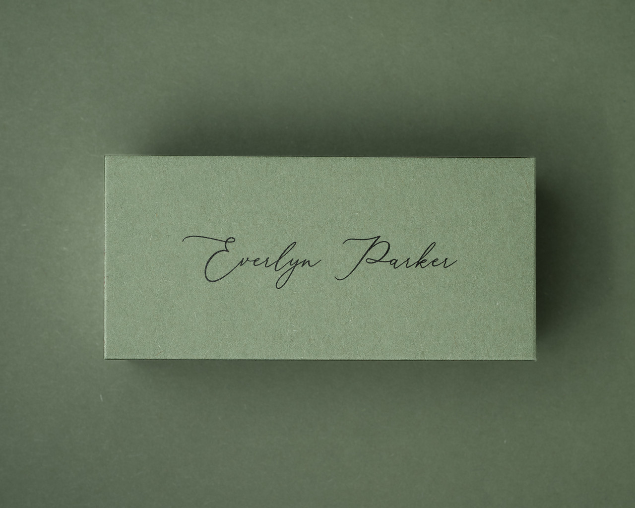 Olive green flat place card with black ink printed name in a modern script font.