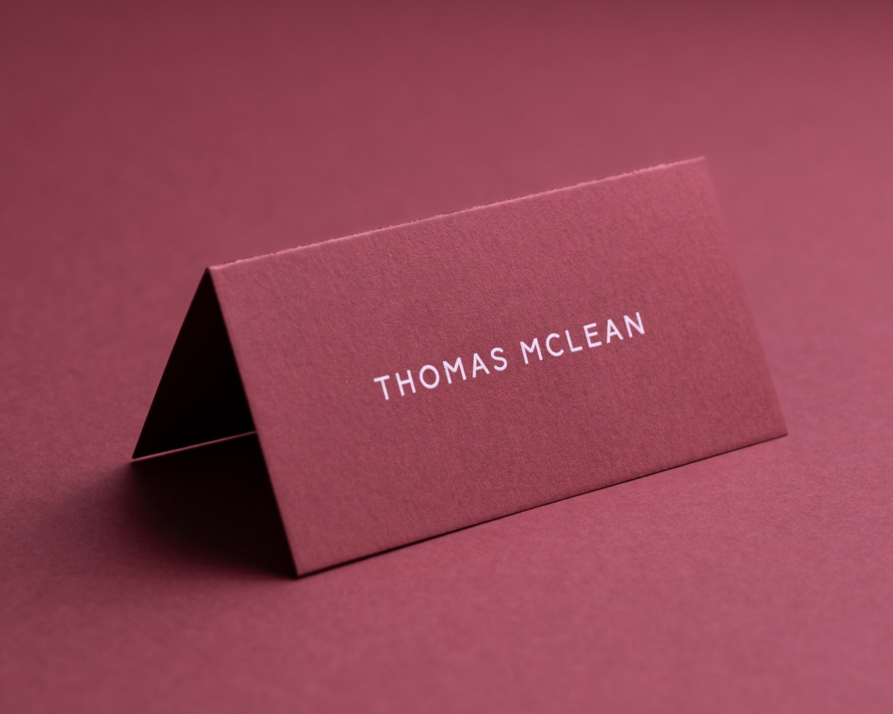 Personalised deep rose folded place card with white ink printing, displaying guest name in a modern font.