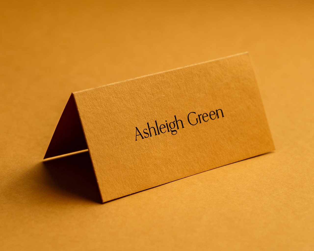 Personalised mustard folded place card with black ink printing, elegant text style.