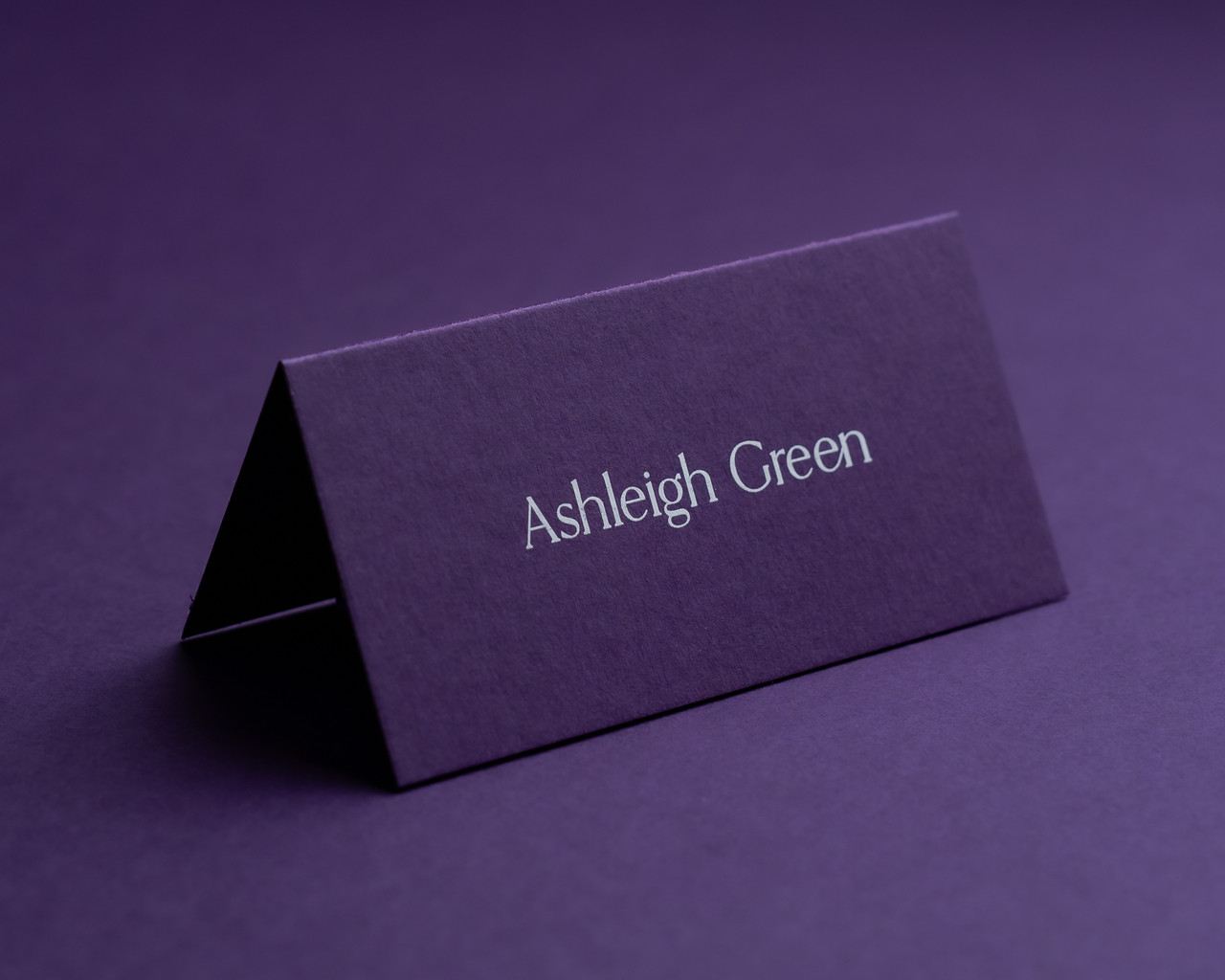 Personalised aubergine folded place card with white ink printing, displaying guest name in elegant font.