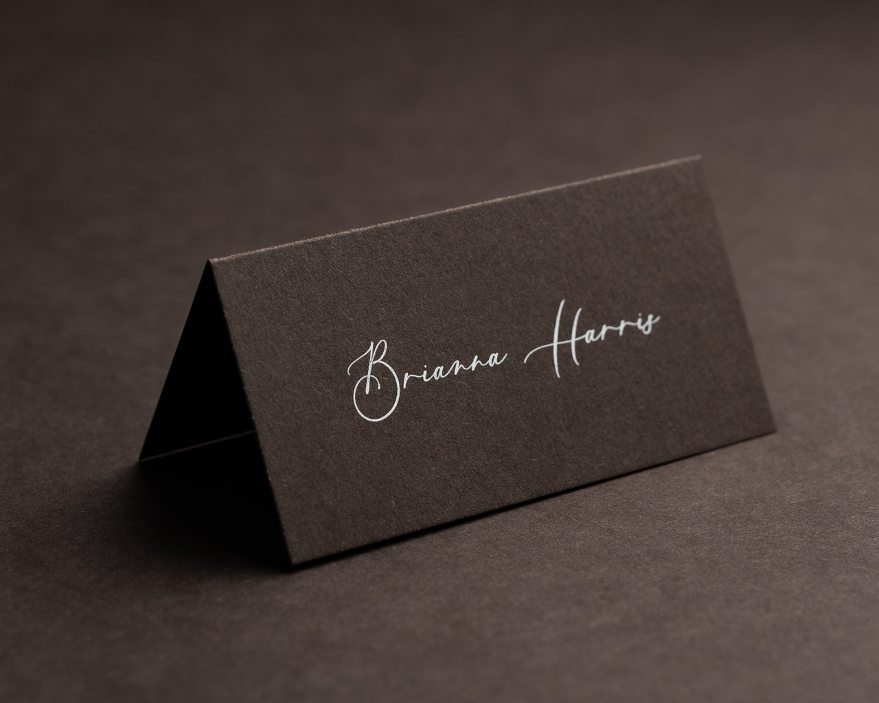 Personalised cocoa folded place card with white ink printing, featuring elegant script text for a formal event.
