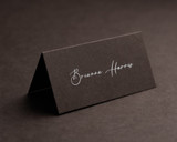 Personalised cocoa folded place card with white ink printing, featuring elegant script text for a formal event.