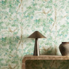 Harlequin Ceibe Pine wallpaper styled in an interior setting, showcasing layered green and blue botanical foliage with soft brown tree detail.