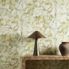 Harlequin Ceibe Nectar wallpaper styled behind a wooden console table, showcasing painterly botanical foliage design in golden green hues.