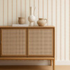 Scion Harvest Stripe Tangerine wallpaper behind a rattan-front cabinet, showing soft orange vertical stripes.