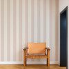 Scion Central Stripe Blush wallpaper styled behind a wooden chair, showcasing soft pink vertical stripe design.