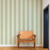 Scion Central Stripe Pea Green wallpaper styled as a feature wall behind a wooden chair, showcasing bold vertical stripe design.