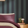 Made Demi Blue Wide Stripe wallpaper styled behind bed with plum bedding and wooden bedside table.
