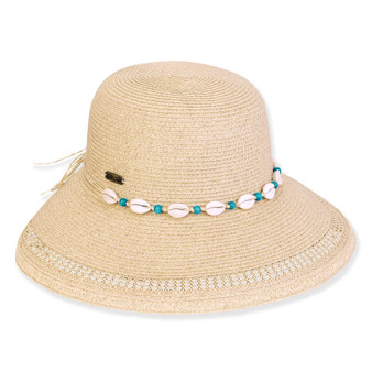 Three-quarter view of a tan woven straw sun hat featuring a rounded crown and a white cowrie shell band.