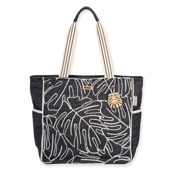 Front view of a rectangular black canvas tote featuring white embroidered monstera leaves, striped handles, and a gold leaf charm.