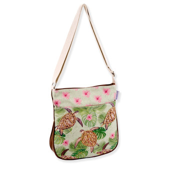 Three-quarter view of a rectangular sage green crossbody featuring printed sea turtles, tropical leaves, pink flowers, and silver metal hardware.