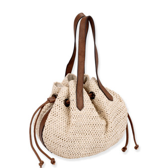 three quarters view of cream crochet Sun N Sand bucket bag featuring brown leather straps, drawstring closure with knotted cord ends.