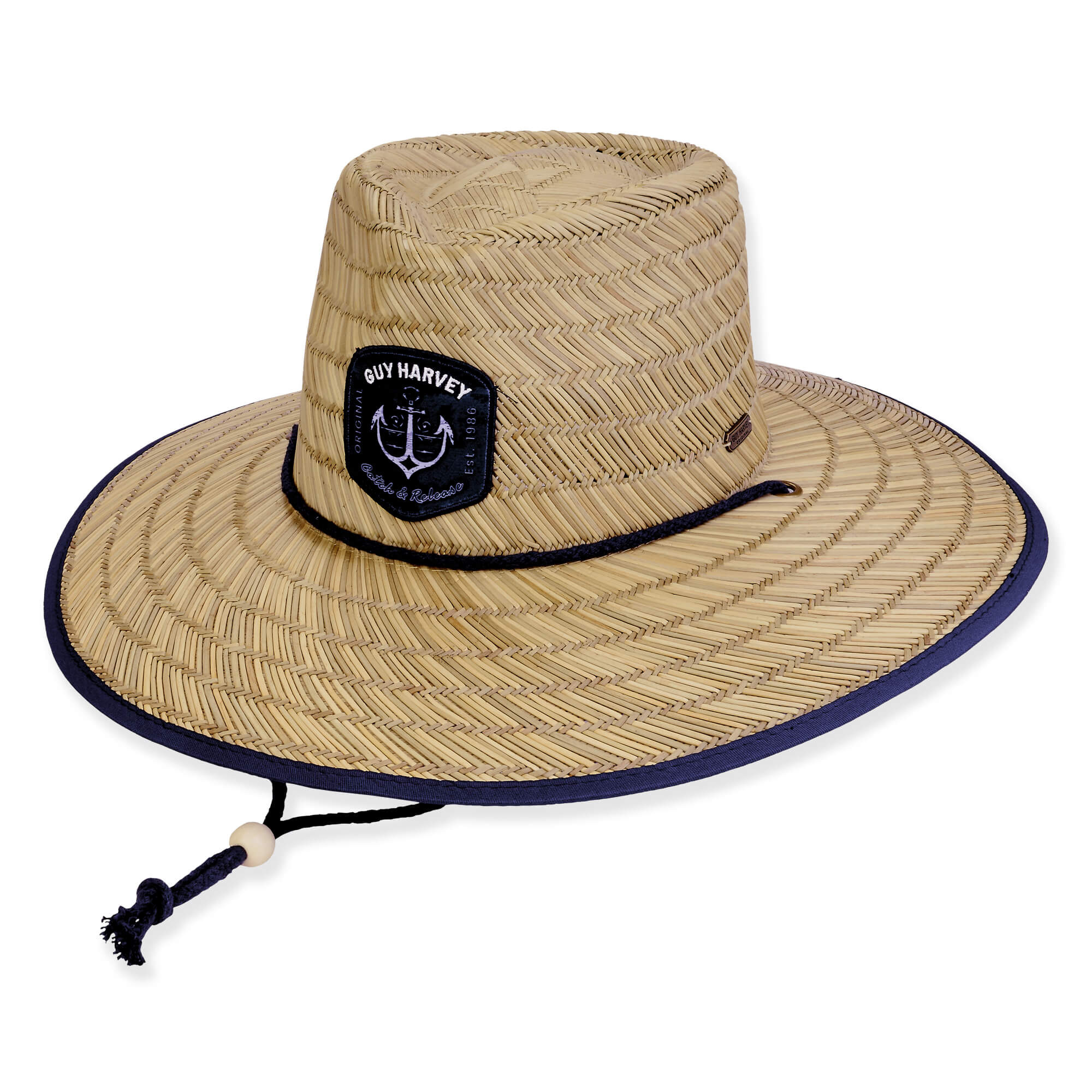 Three-quarter view of a natural straw lifeguard hat featuring a Guy Harvey anchor patch, blue bound brim, and adjustable chin cord.