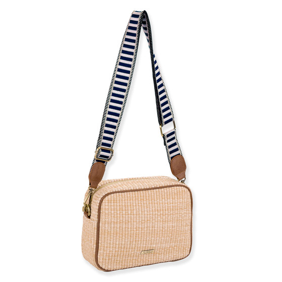 Three-quarter view of a rectangular beige woven straw crossbody camera bag featuring brown leather trim and a blue-striped canvas strap.
