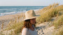 Lifestyle profile portrait of the Sun N Sand HH3606 Women’s Safari Hat in a natural woven straw, featuring a decorative beaded hatband with turquoise and white accents and a structured flat brim with a pinched crown for an adjustable fit.