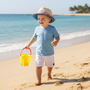 Lifestyle beach shot of the Sun N Sand HK570 kids' straw hat in a natural tan with a blue patterned brim, featuring a classic fedora crown and a wide sun-shielding brim for stylish UV protection during seaside adventures.