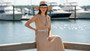 Lifestyle portrait of the Sun N Sand HH3624 A Women’s Safari Hat in a natural woven straw, featuring a decorative braided leather-style hatband with metallic accents and a wide, structured flat brim with a pinched crown for an adjustable fit and UPF 50+ sun protection.