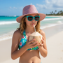 Lifestyle beach shot of the Sun N Sand HK563 kids' sun hat in a shimmering pink woven pattern, featuring a classic fedora-style crown and a protective mid-sized brim for chic sun safety at the shore