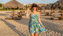 Lifestyle portrait of the Sun N Sand HH3630 Women’s Bucket Hat in a natural tan woven straw, featuring a decorative blue and white patterned hatband with a side metallic brand plate and a structured down-sloping brim for an adjustable fit and UPF 50+ sun