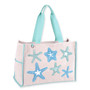 Three-quarter view of a rectangular beige canvas tote bag featuring embroidered starfish, colorful contrast trim, wide fabric handles, and metal hardware.