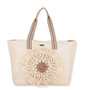 Front view of light straw tote with striped handles, layered circular sunburst front detail, and textured woven body highlighting artisanal summer design.