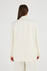 Profile view of model wearing the Oroton Double Breasted Blazer in Cream and 53% Polyester 43% Wool 4% Elastane for Women