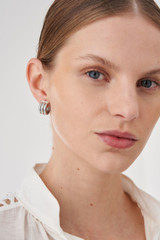 Profile view of model wearing the Oroton Drew Mini Hoops in Silver and Brass Base Metal With Rhodium Plating for Women