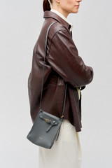 Profile view of model wearing the Oroton Margot Tiny Bucket Bag in Dark Slate and Pebble leather for Women . IP:3