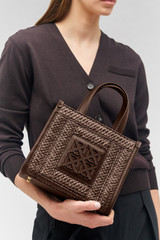 Profile view of model wearing the Oroton Lane Straw Small Tote in Mahogany and Woven straw with leather trims for Women . IP:2