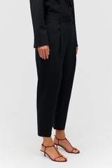 Profile view of model wearing the Oroton Tapered Pleat Pant in Black and 98% wool 2% elastane material for Women . IP:4