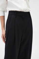Profile view of model wearing the Oroton Tapered Pleat Pant in Black and 100% wool fabric for Women . IP:4
