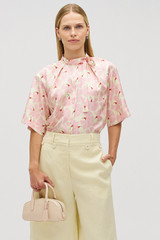 Profile view of model wearing the Oroton Fan Flower Tie Neck Blouse in Peony and 100% silk for Women .