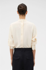 Profile view of model wearing the Oroton Fluid Cutwork Long Sleeve Top in Antique White and 75% acetate and 25% polyester blend fabric for Women . IP:5