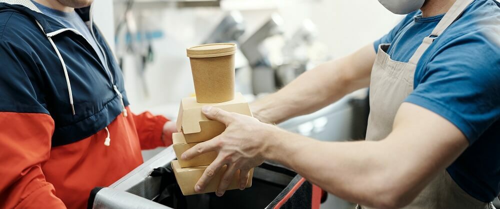 Person handloing compostable packaging to delivery driver