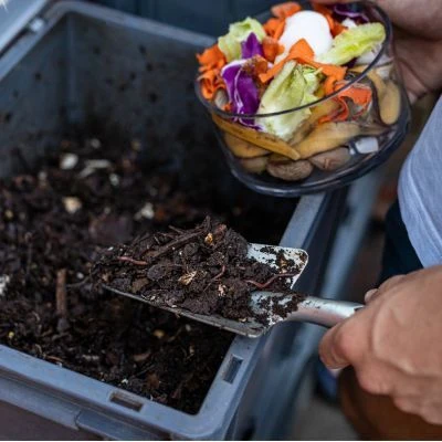 man putting compost in a bin with shovel
