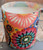 This candle is covered with a bright multi colored fabric of flowers
