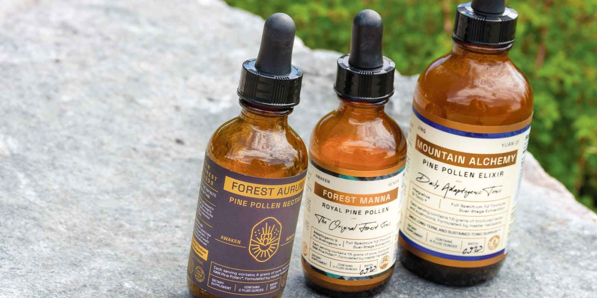 Three RAW Forest Foods Pine Pollen Tinctures on stone—Forest Aurum Pine Pollen Nectar Tincture, Forest Manna Royal Pine Pollen Tincture, and Mountain Alchemy Pine Pollen Elixir Tincture