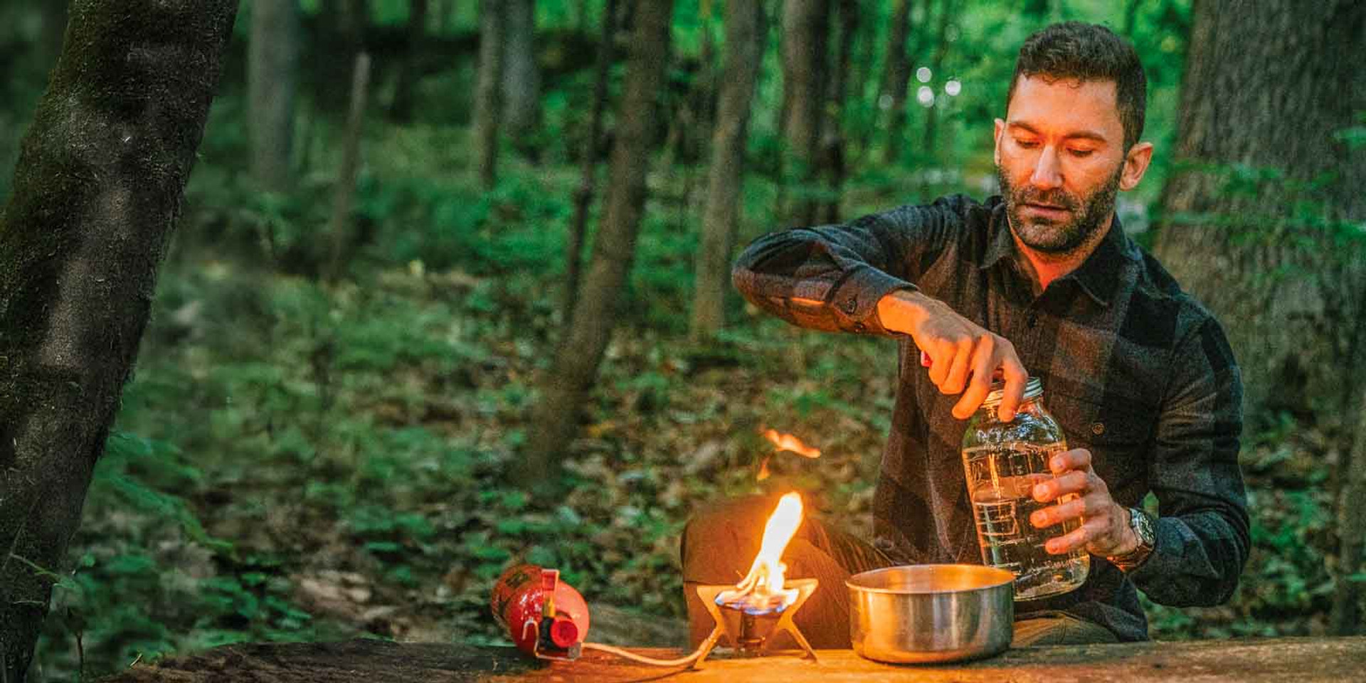 RAW Forest Foods’ founder preparing herbal decoction in forest with flame stove and mason jar