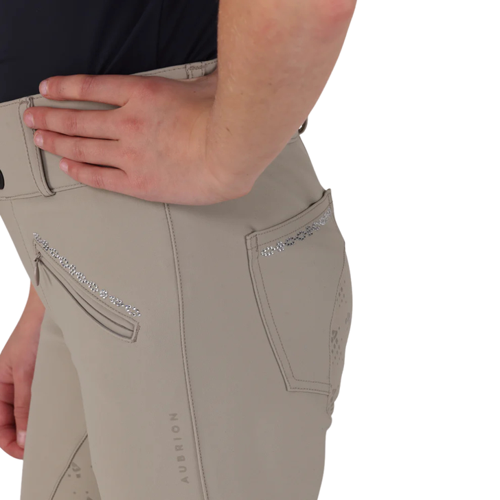 Aubrion Optima young rider breeches are created for elite competition performance using modern design technology, innovative fabrics, and championship ready styling, appealing to riders who demand excellence whilst training or competing. Anatomically cut for the best athletic fit, moisture wicking technology is incorporated into superior figure-enhancing fabric that yields with the rider whilst maintaining a polished, competition-ready look. Sleek LX streamlines detail to draw attention to its standout feature: eye-catching iridescent diamante chains, interlinked and set at the pocket edges for a sophisticated, radiant finish. The legs taper to low profile cuffs for a smooth fit under long riding boots. Neatly finished with a self-colour Aubrion logo at the leg, adding a subtle nod to elevated equestrian design.
