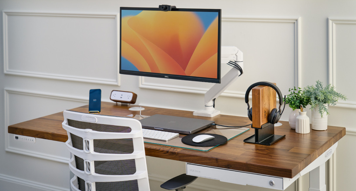 Uplift standing desk in a bright office setting with monitor, accessories, and seated user