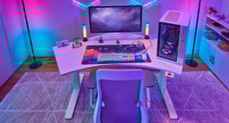 High-angle view of a 120-Degree UPLIFT Desk with a white top. Full gaming setup, PC, monitor, and bright RGB accessories