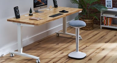 UPLIFT Standing Desk with white frame and Birch Butcher Block top in an office setting with a Cobalt Blue Engage Stool 