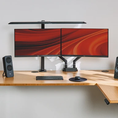 Zilker Dual Monitor Arm in black clamped to an UPLIFT L-Shaped Standing Desk with a Bamboo desktop