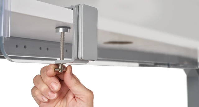 Close-up of a hand tightening a clamp screw under a desk surface with metal hardware