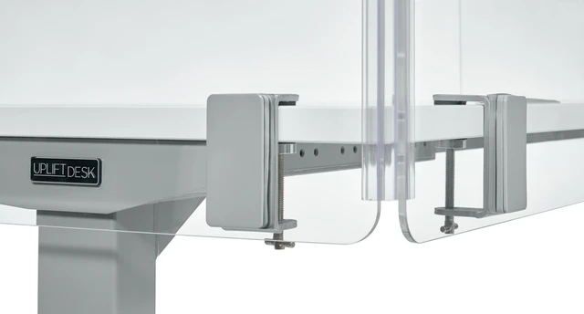 Close-up of the metal clamp and beam assembly on a white desk frame labeled 'UPLIFT DESK' with adjustable joints