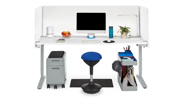 A white office desk setup with a computer, blue stool, and storage drawer on the left; a rolling pedestal under the desk and a cubby organizer on the right