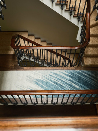David Rockwell Splash Sea Runner seen from above on a staircase landing, framed by a mahogany handrail and iron balusters