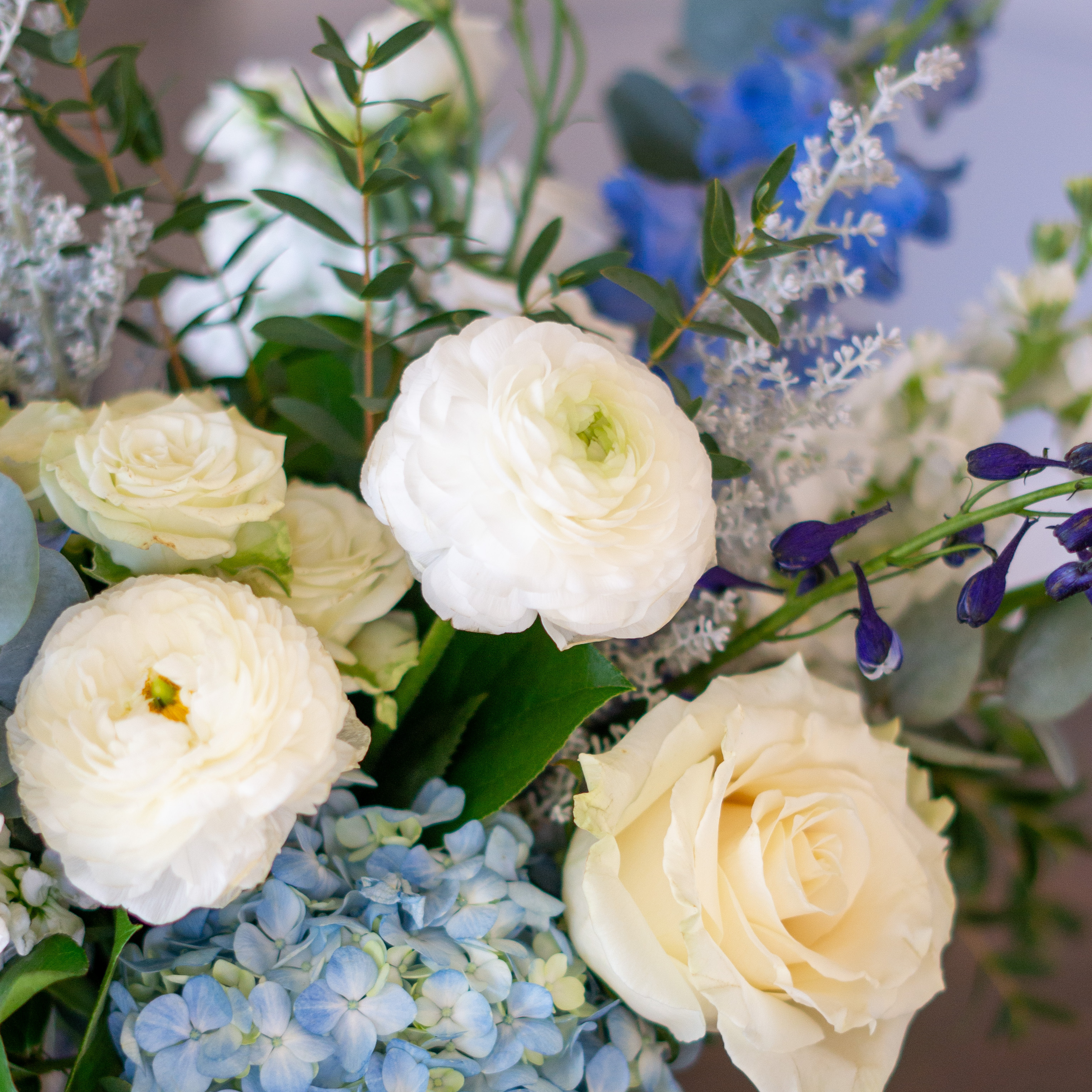 Peach valentines day flowers on a blue tablecloth. Flowers include peach roses, cream lisianthus, peach stock, white hydrangea, pink spray roses, and pink hypericum berries accented with eucalyptus. 