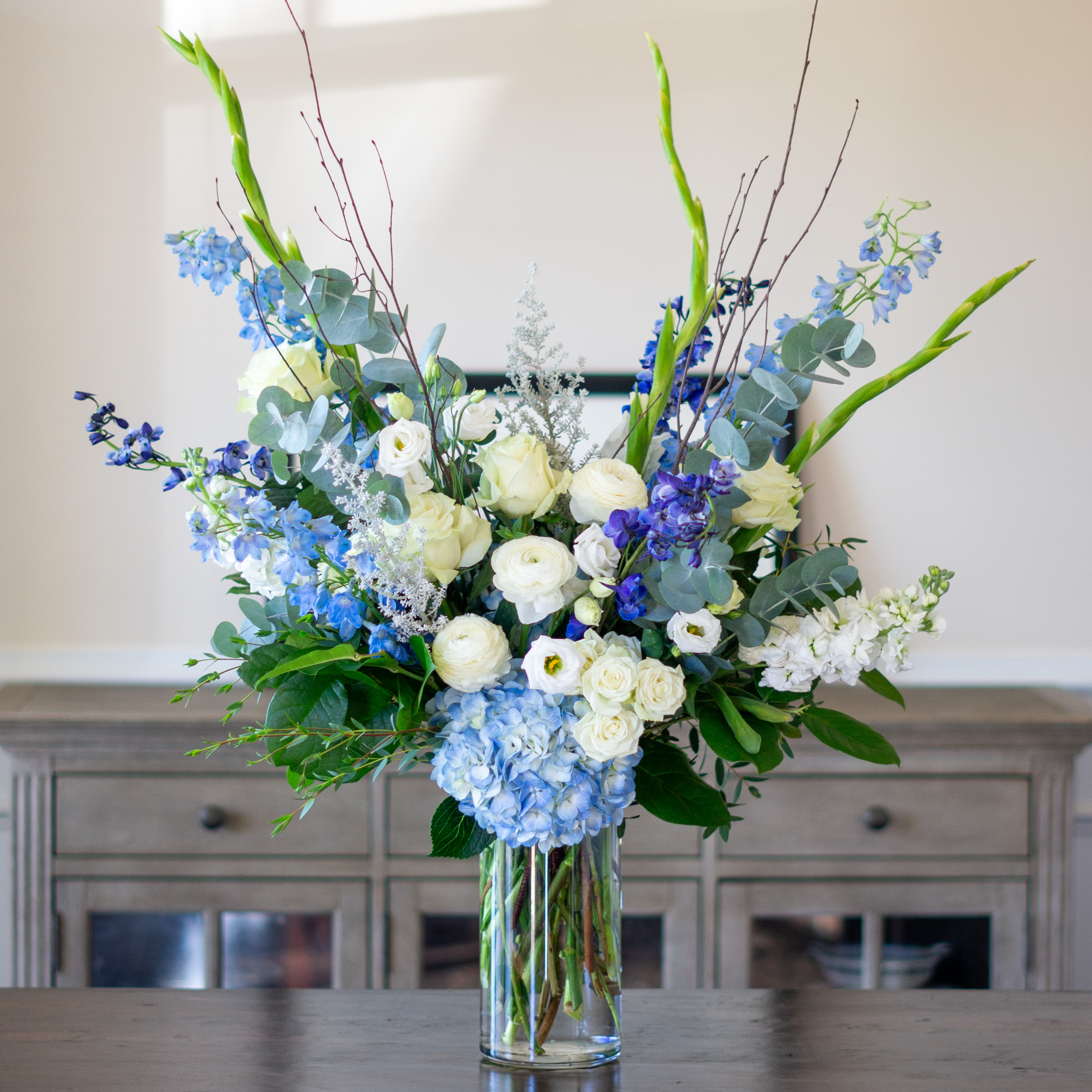 Peach valentines day flowers on a blue tablecloth. Flowers include peach roses, cream lisianthus, peach stock, white hydrangea, pink spray roses, and pink hypericum berries accented with eucalyptus. 